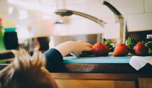 a child trying to reach strawberries on a kitchen surface